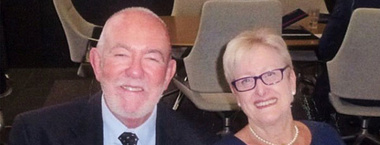 Janne and Tony looking at the camera, smiling. Tony is wearing a suit and tie, while Janne wears navy blue with matching glasses and pearl jewellery.