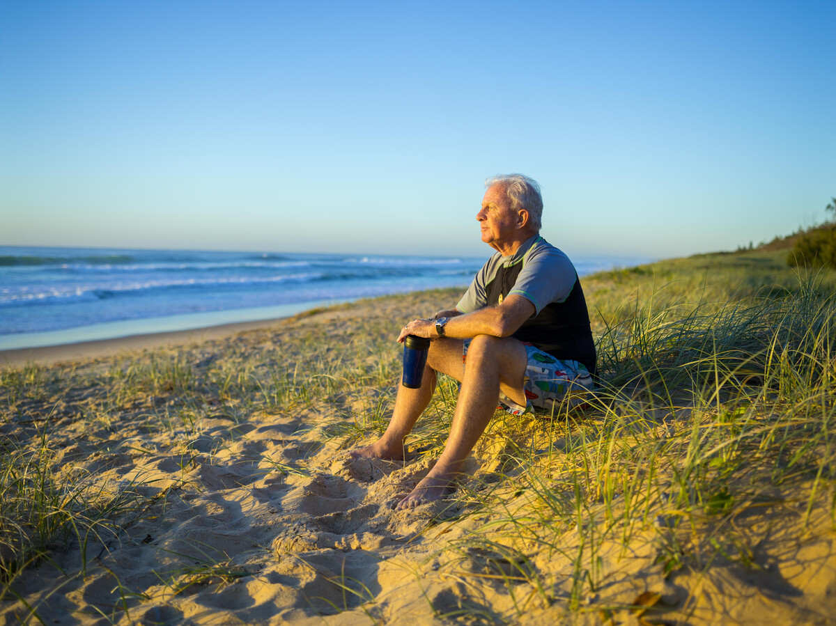 A man sitting on sand dunes looking out over beach to ocean