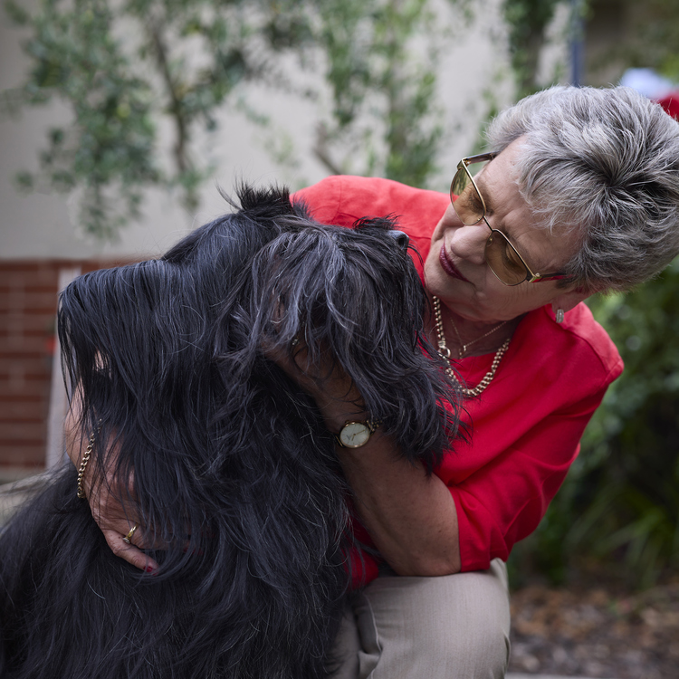An elderly lady cuddling her furry black dog