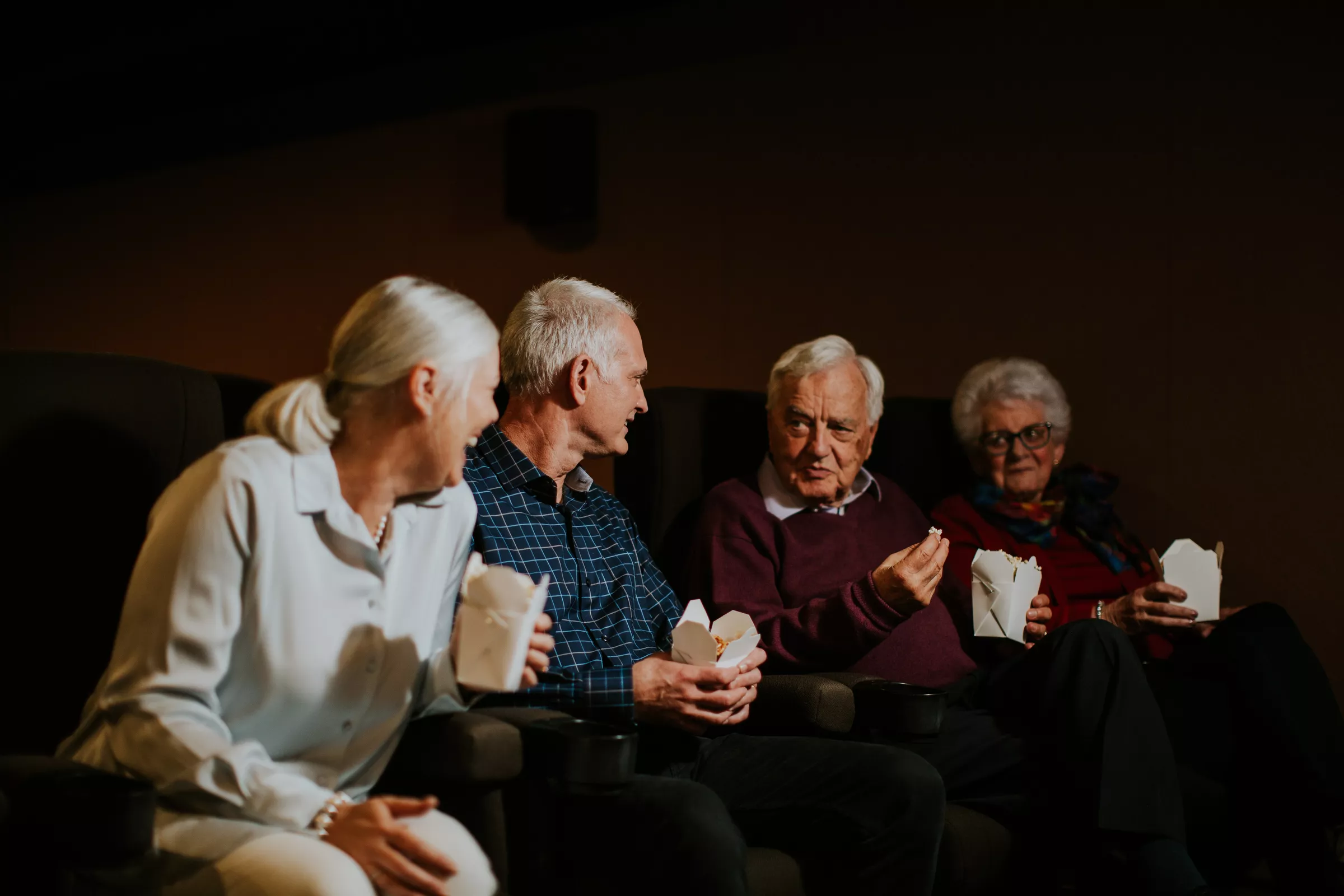 Four senior people eating popcorn and chatting at the movies
