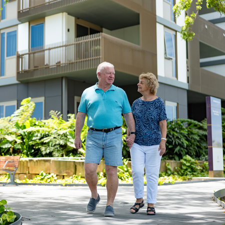 A couple holding hands and walking around an urban retirement village in Brisbane
