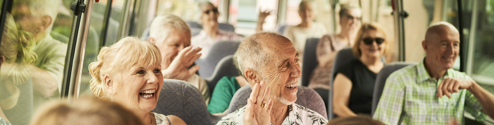 A group of retirees sitting on a bus and smiling