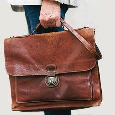 A close-up of a stylish but worn-out brown leather briefcase held by a man’s hand.