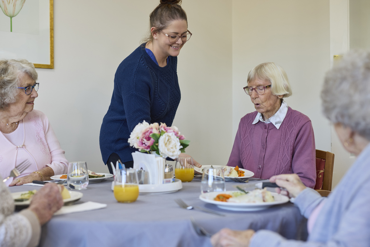 A help serving a meal to a group of older residents 