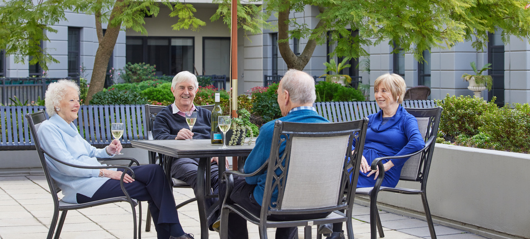 Four seniors sitting at an outside table enjoying a glass of wine