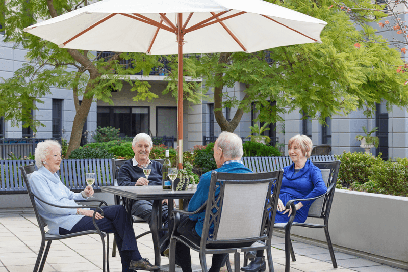 Four seniors sitting at an outside table enjoying a glass of wine