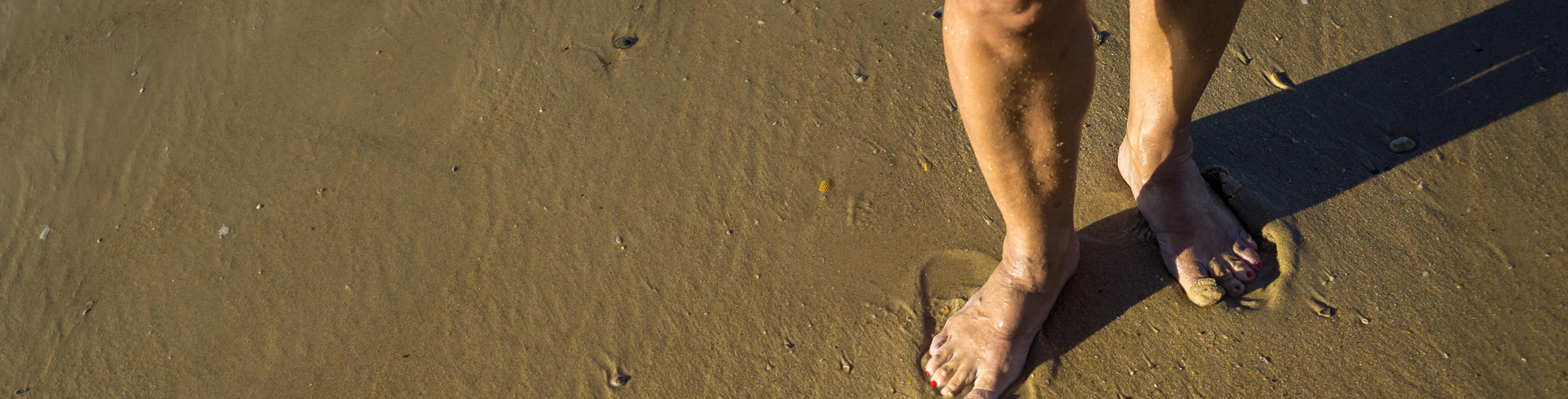 Close up image of woman's bare feet walking on wet sand.