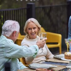 Two retirement village residents sitting outside at a dinner party and sharing a glass to drink