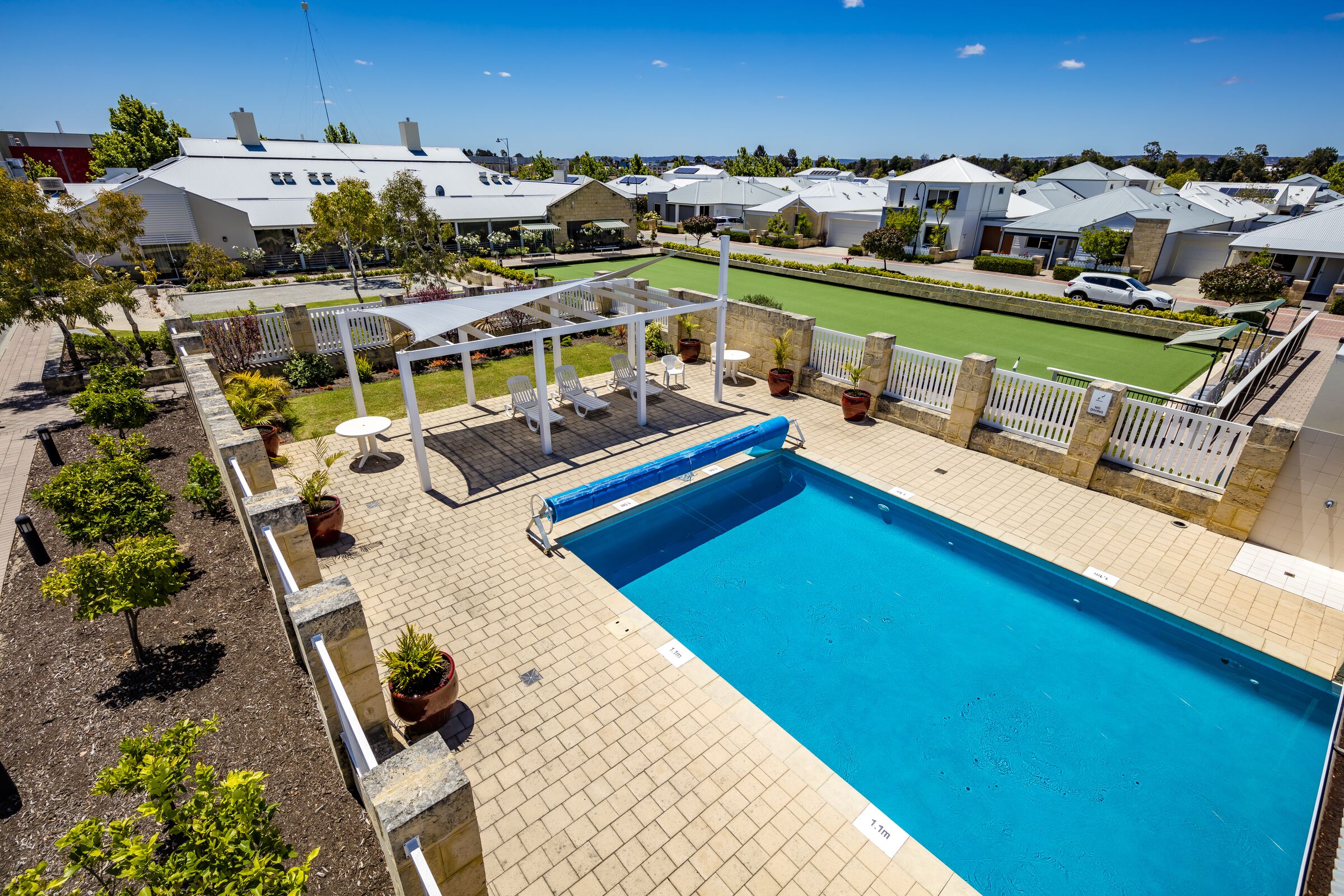 Parkland Villas Ellenbrook aerial image of outdoor swimming pool with shaded poolside seating and lounges next to bowling green