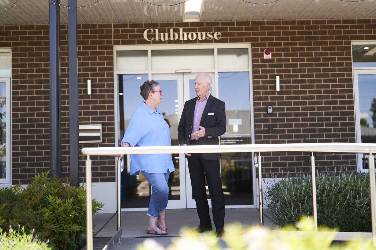 A resident and Village manager  standing and chatting in front of the clubhouse