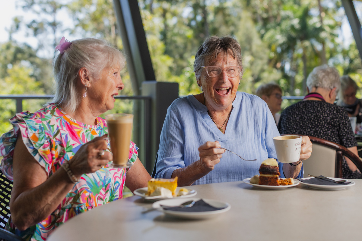 Buderim Gardens residents Gaye and Karen having drinks and cake in the retirement village café while laughing