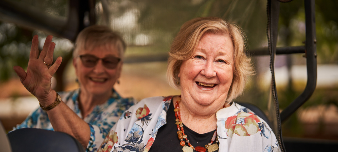 Two female residents of Brentwood Village smiling and driving in the village buggy