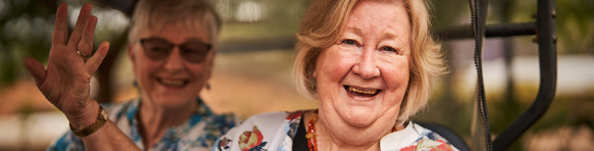 Two female residents of Brentwood Village smiling and driving in the village buggy