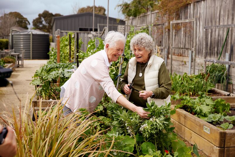 Two ladies working in the garden beds at a village