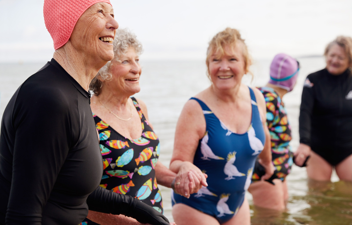 Four seniors in their swimwear are holding each other's hand and smiling
