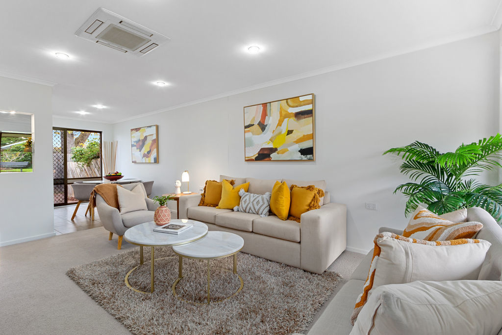 A neutral-toned living room with beige and yellow cushions, warm-toned artwork on the walls and a soft brown faux fur rug adding texture and warmth to the space