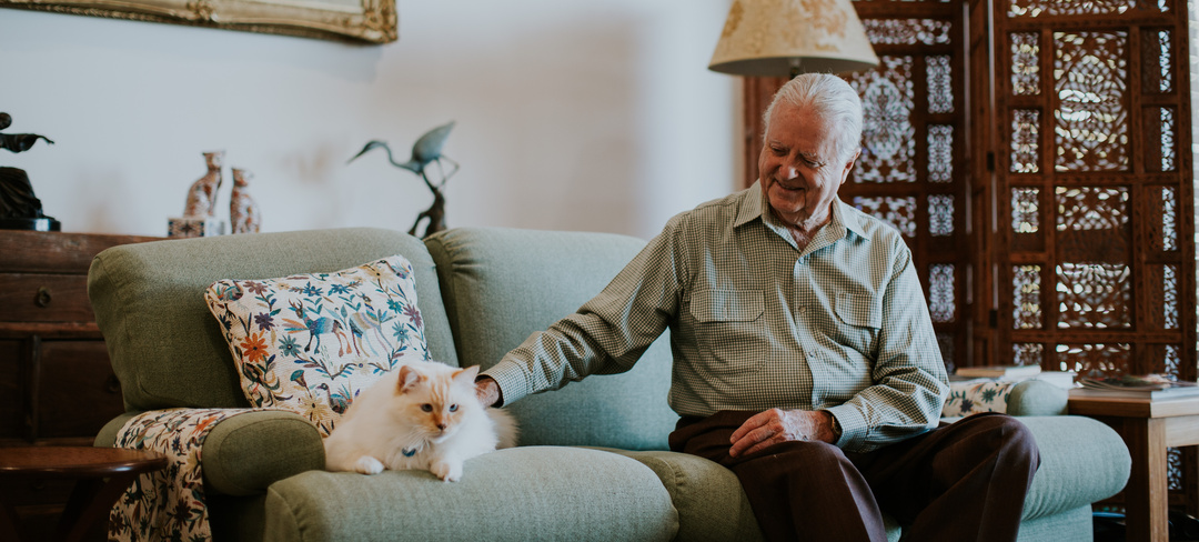 Senior man petting his cat on the couch in pet friendly environment