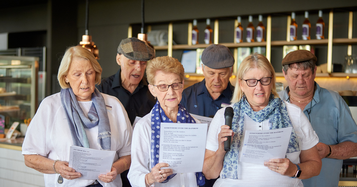 A group of seniors singing together, each holding a sheet of music.