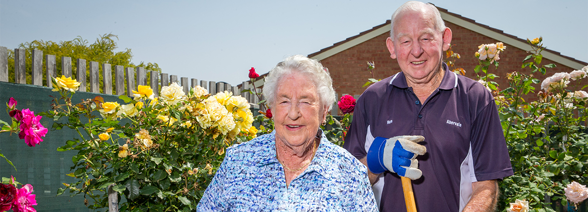 residents Joan and Ron smiling at the camera posing in front of the garden