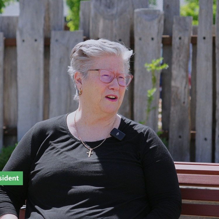 an old woman looking and smiling at the camera sitting on the bench outside