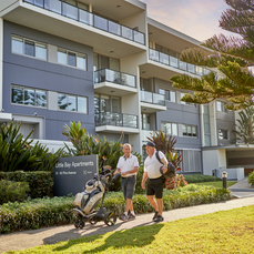 Two men walking through an apartment retirement village carrying golfing equipment