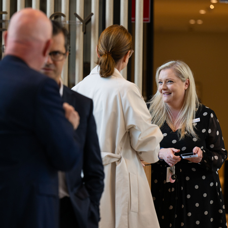 Kate wearing a polka dotted dress and talking to a guest at the Grand Opening ceremony of Ardency Kennedy Place