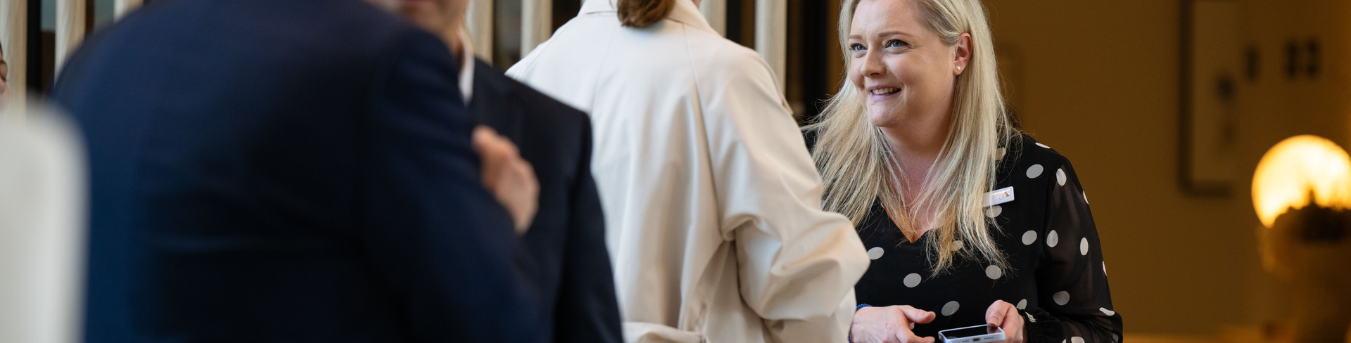 Kate wearing a polka dotted dress and talking to a guest at the Grand Opening ceremony of Ardency Kennedy Place