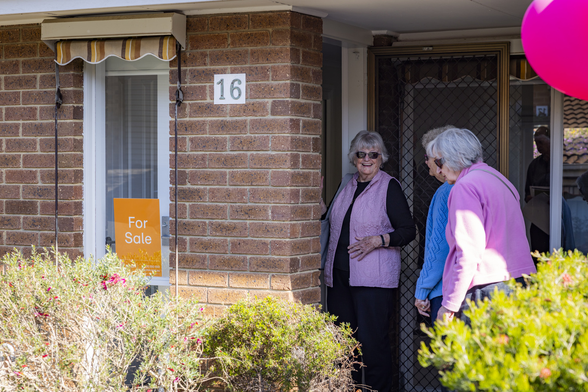 Three elderly ladies entering a house that is for sale with balloons out front