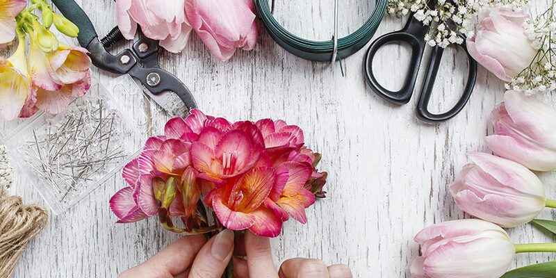 A florist hands cutting flowers on the desk with scissors and plants around