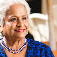 Retirement village resident Satya Prema Naidu is smiling, wearing a striking blue and black patterned top with a blue and white beaded necklace and pearl drop earrings.