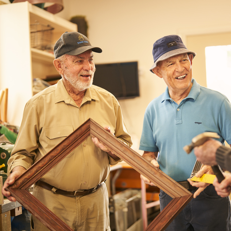 Three residents holding a wooden frame and a hammer discussing their handy work