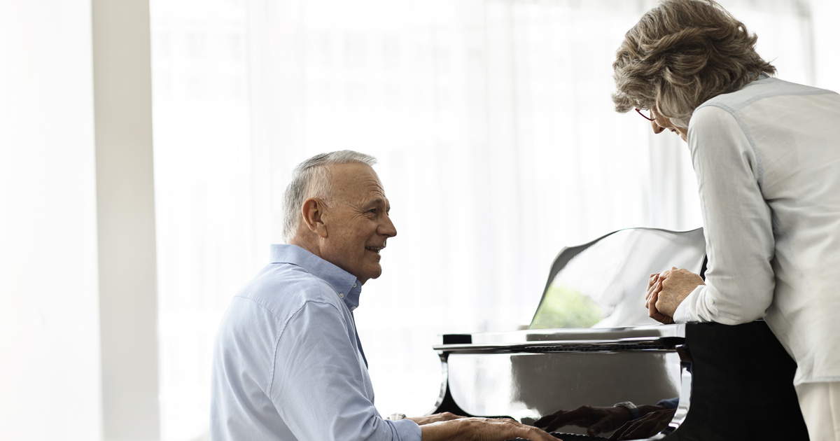 Senior man playing the piano with a senior woman watching