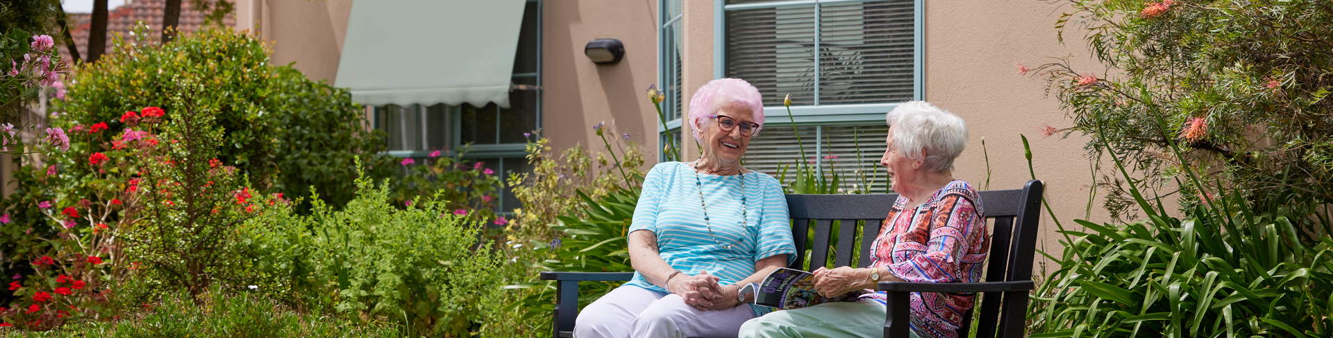 Two elderly ladies sitting on a bench in front of a retirement village