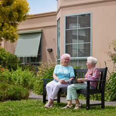 Two elderly ladies sitting on a bench in front of a retirement village