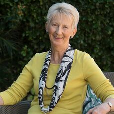 Retirement village resident Irene Baldwin wears a yellow top and a striking black and white scarf. She sits in a lush garden at Allora Gardens, Queensland.