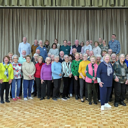 a group of volunteer residents standing in two rows in the village community centre and smiling for the camera