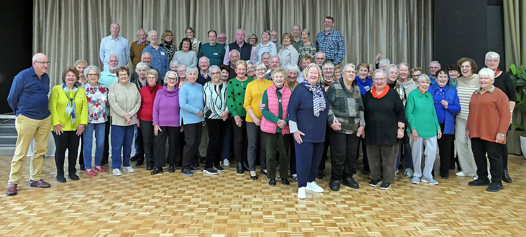 a group of volunteer residents standing in two rows in the village community centre and smiling for the camera