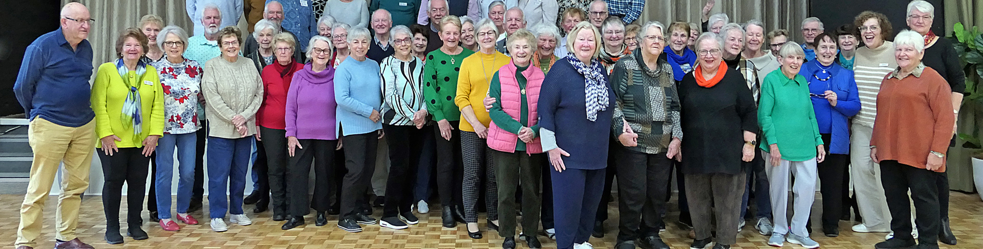 a group of volunteer residents standing in two rows in the village community centre and smiling for the camera