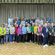 a group of volunteer residents standing in two rows in the village community centre and smiling for the camera