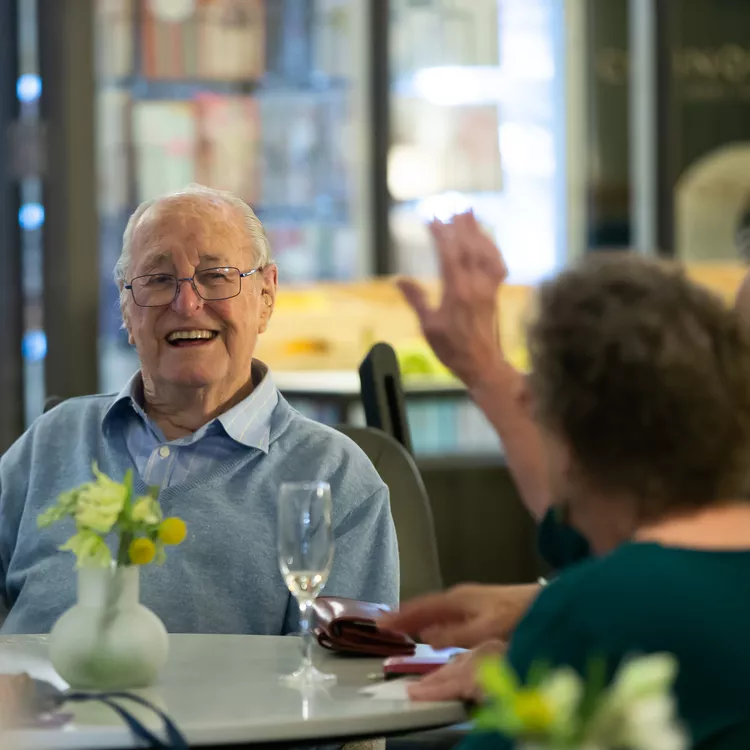 An elderly gentleman sitting at a table with other retirement village residents and laughing