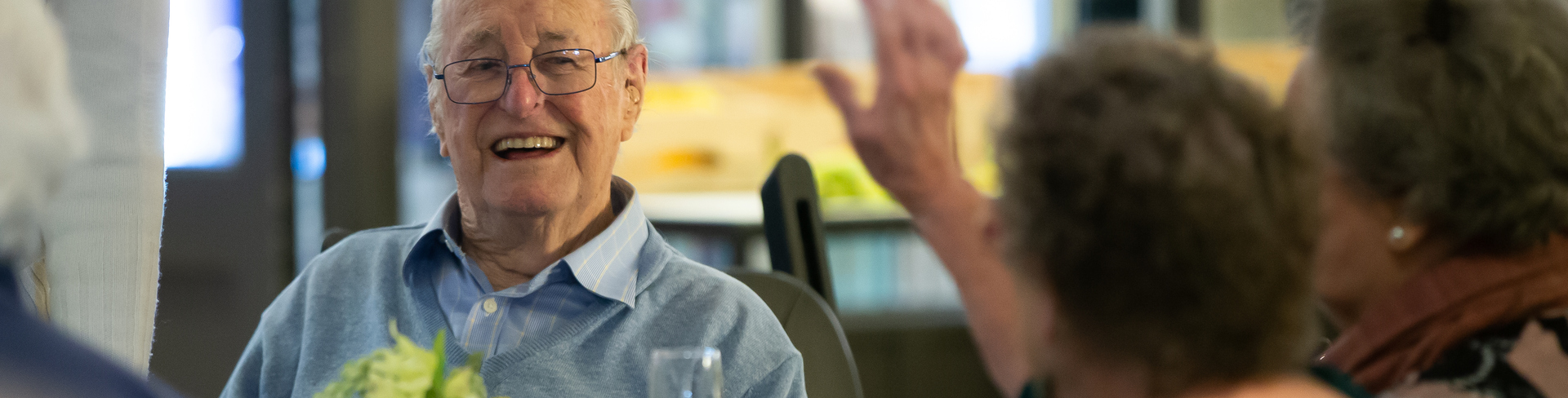 An elderly gentleman sitting at a table with other retirement village residents and laughing