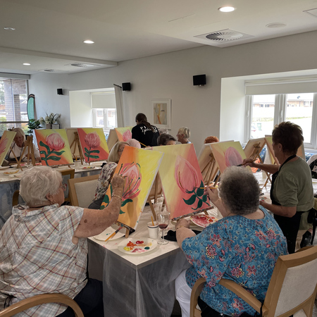 A senior lady painting while the teacher look on.