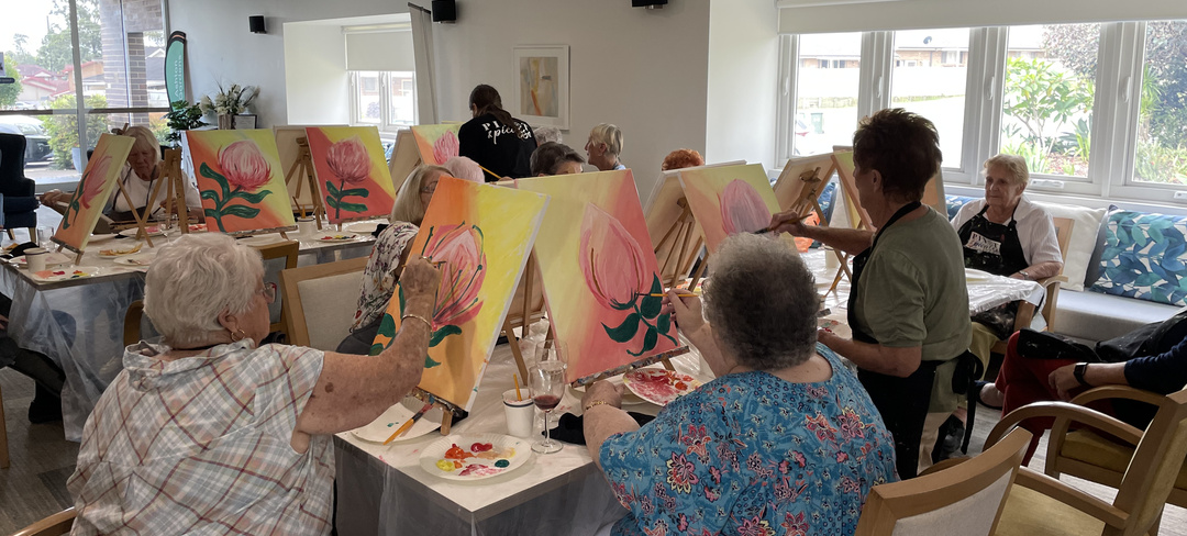 A senior lady painting while the teacher look on.