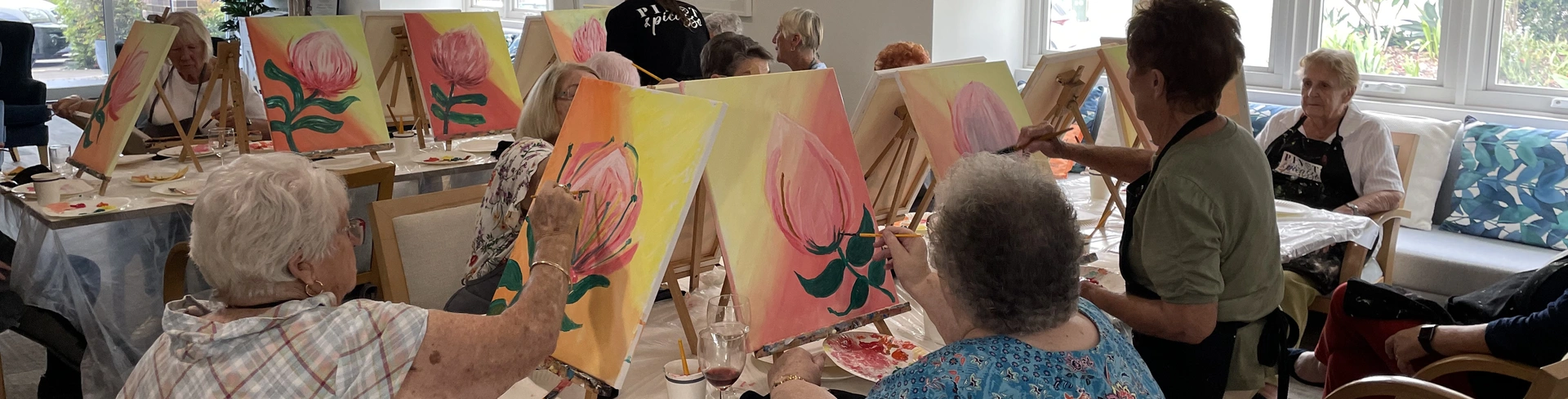 A senior lady painting while the teacher look on.