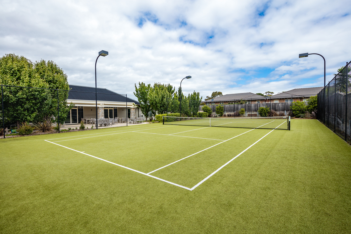 Martha's Point grass tennis court with night lighting surrounded by village buildings