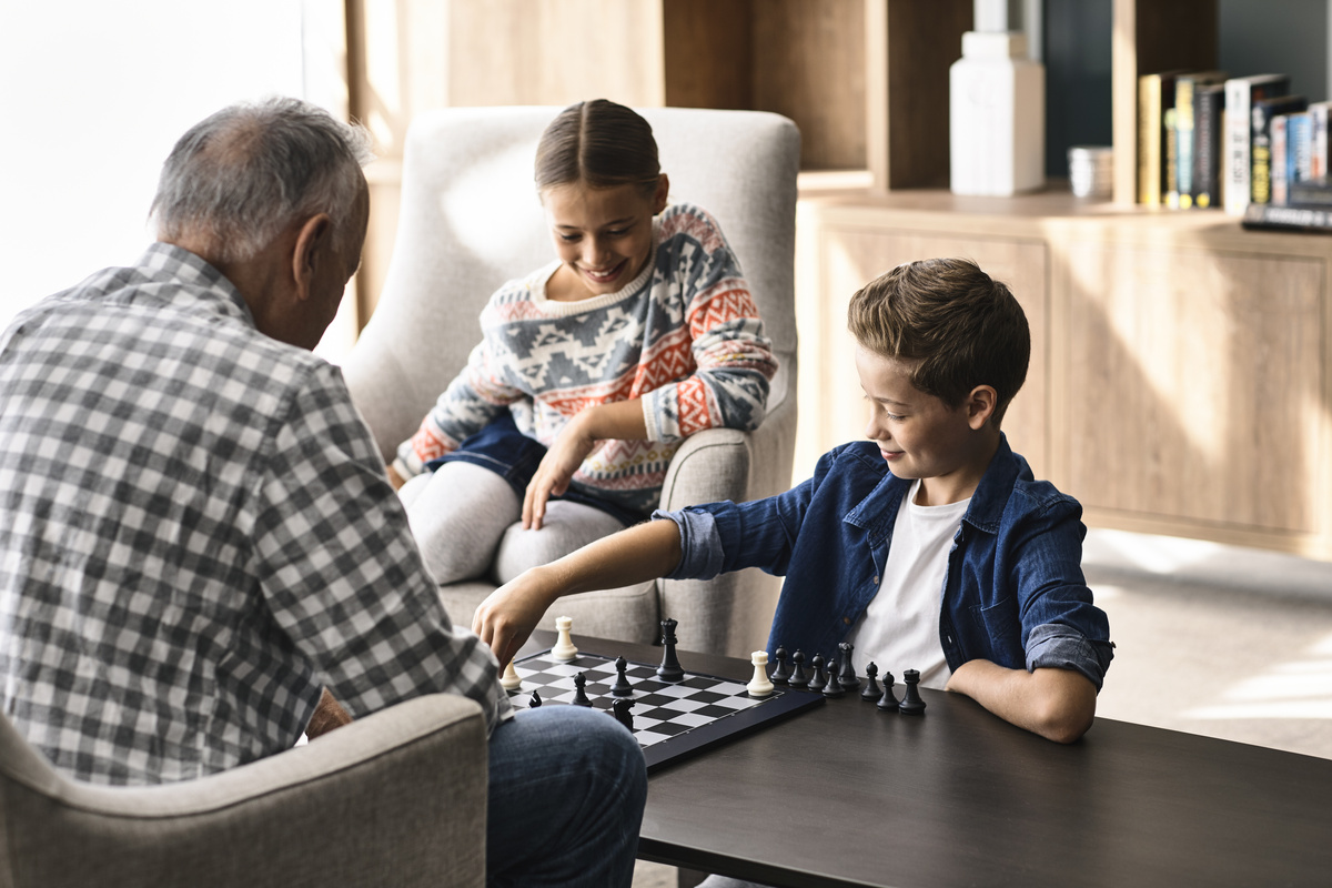 A grandfather playing chess with his two grand children at a retirement village