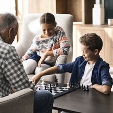 Two children playing chess with an older man. 