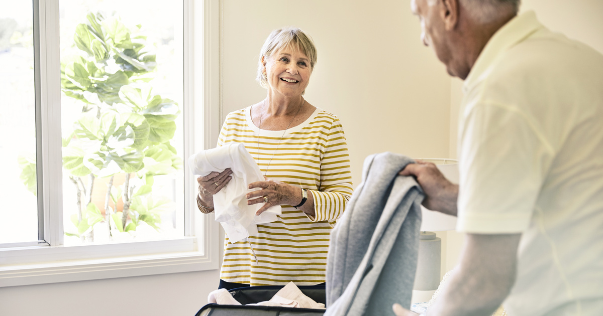 Happy senior couple packing suitcases on the bed