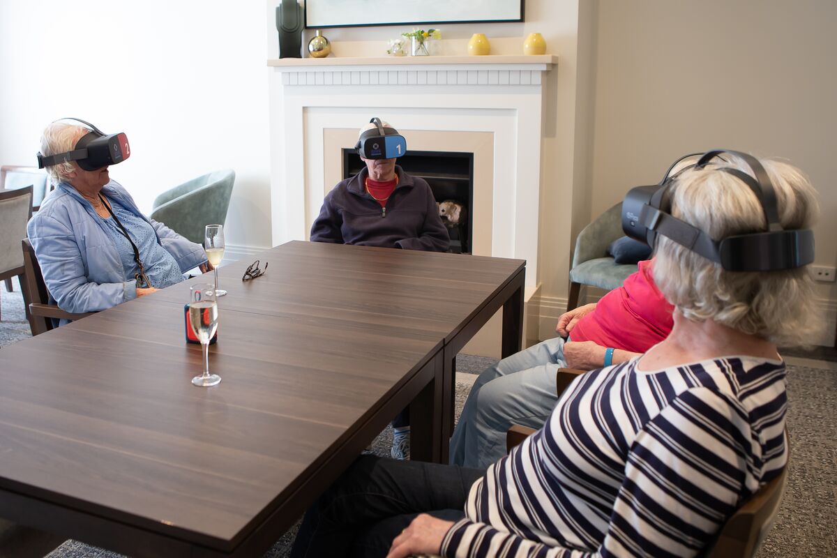 Four ladies sitting on a desk in a retirement village with VR glasses taking a virtual trip