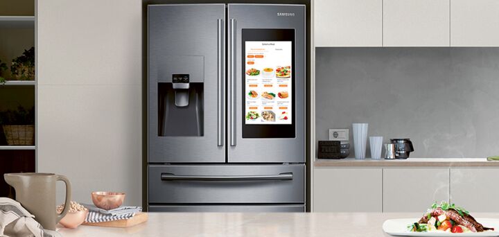 A high-tech fridge sits in a modern-looking kitchen. The fridge has a screen featuring online recipes and internet connectivity. 